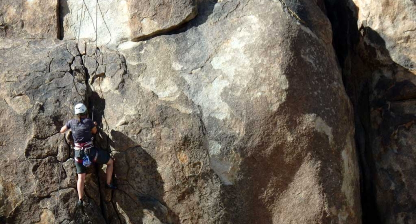 A person wearing safety gear is secured by ropes as they climb a rock face. 